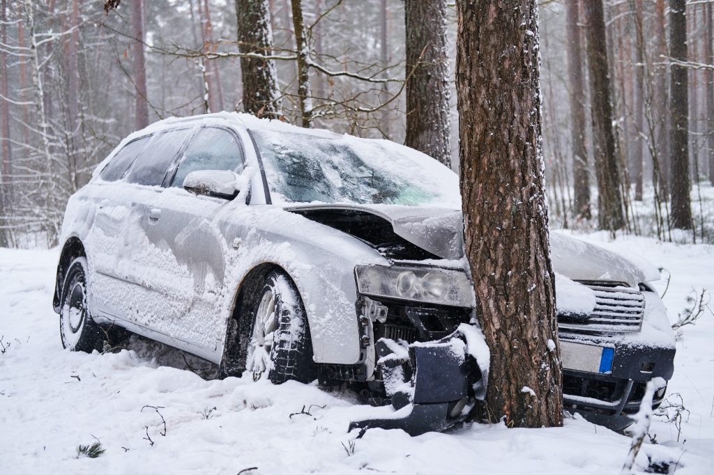 Broken car crashes into tree after losing control on slippery road in snowy forest.